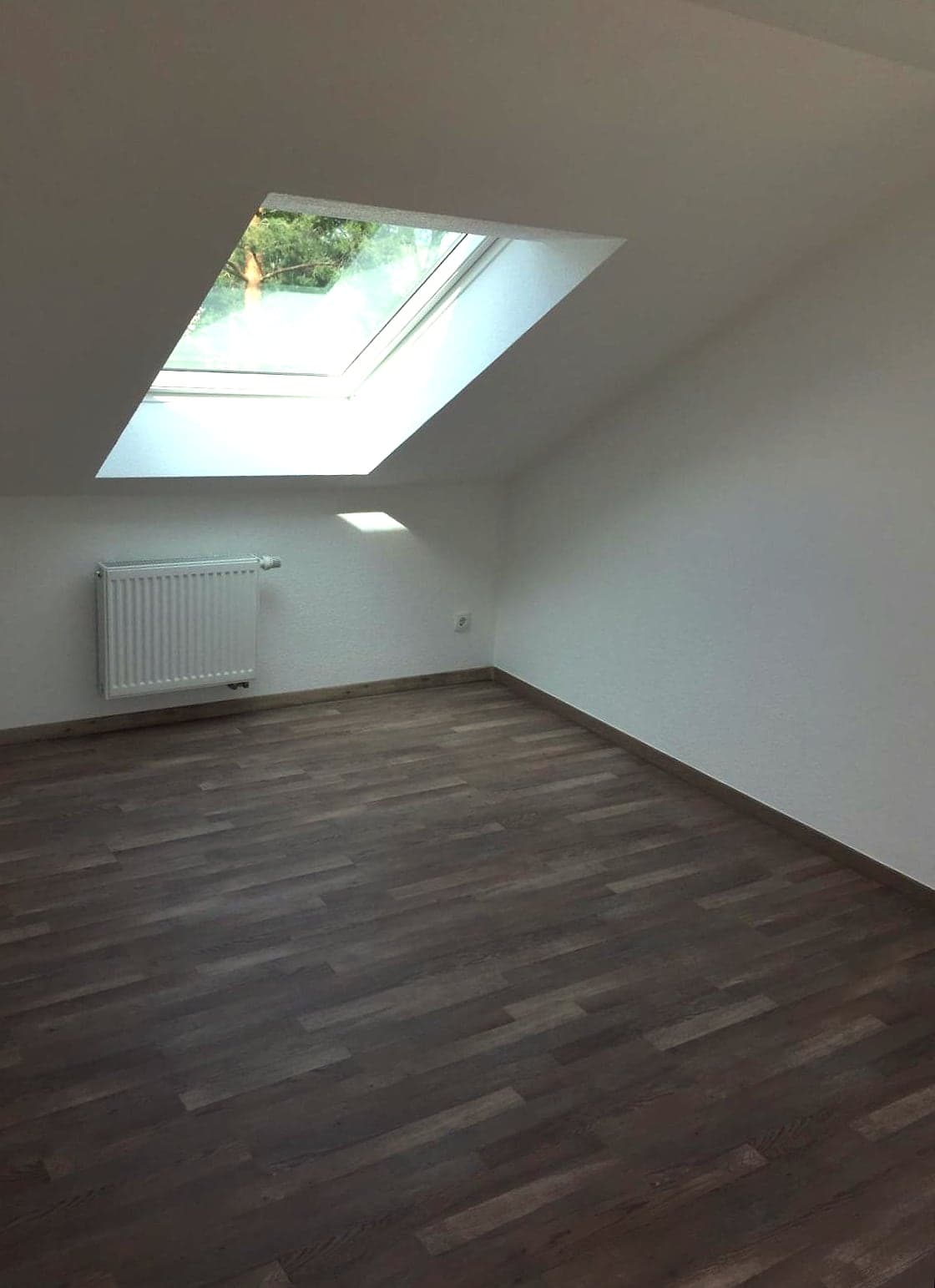 Fertig renoviertes Dachzimmer mit Dachfenster, hellen Wänden und neu verlegtem Holzboden