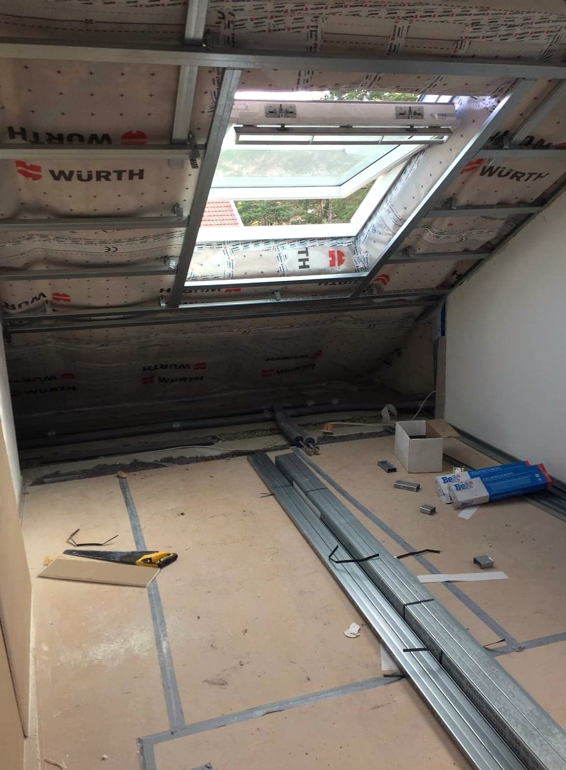 Dachgeschoss im Rohbau: Metall-Ständerwerk unter der Dachschräge, Unterspannbahn, Dachfenster und Werkzeug auf dem Boden