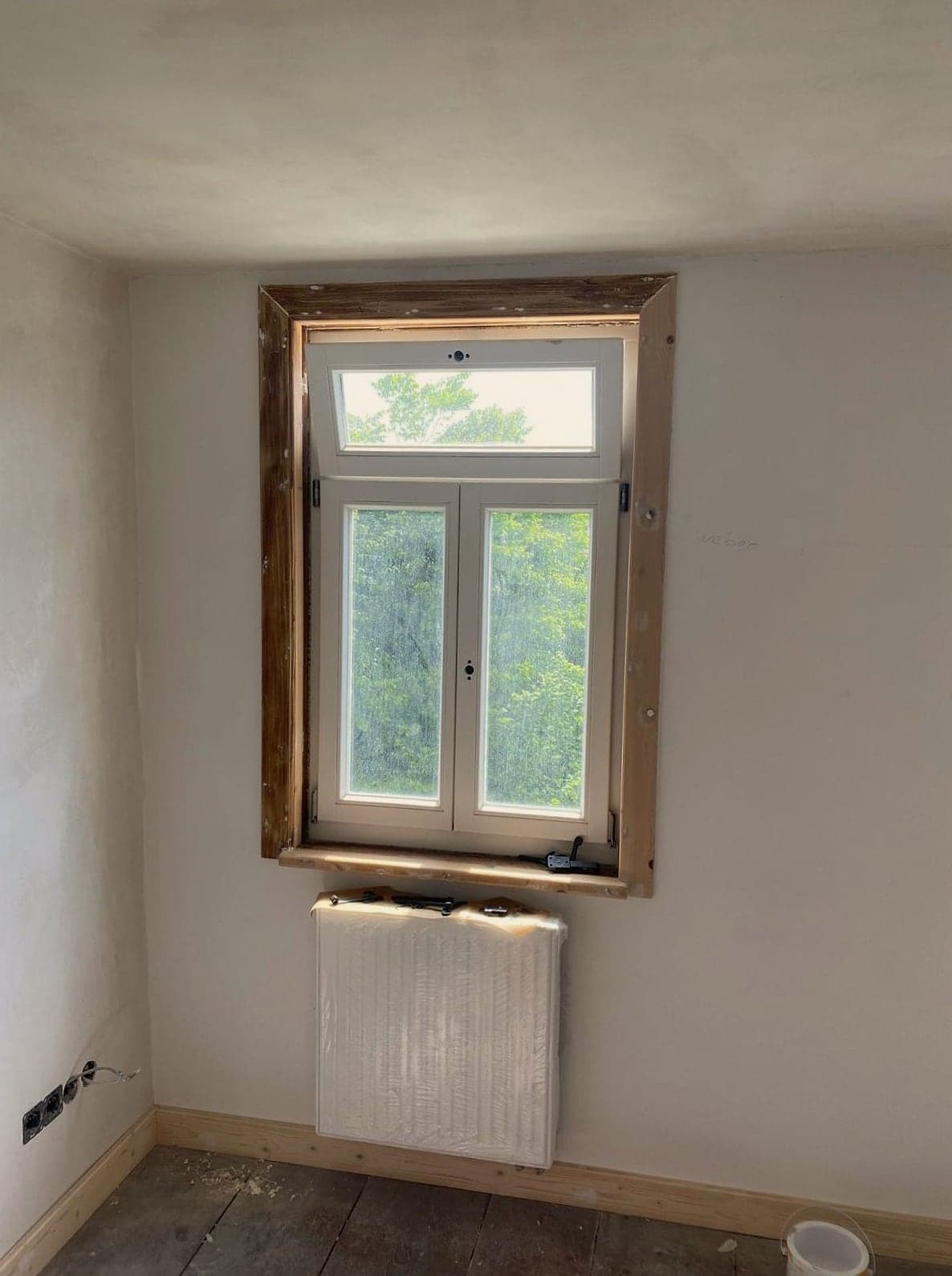 Frisch verputzter Raum mit freigelegtem Kastenfenster und neuem Heizkörper unter der Fensterbank
