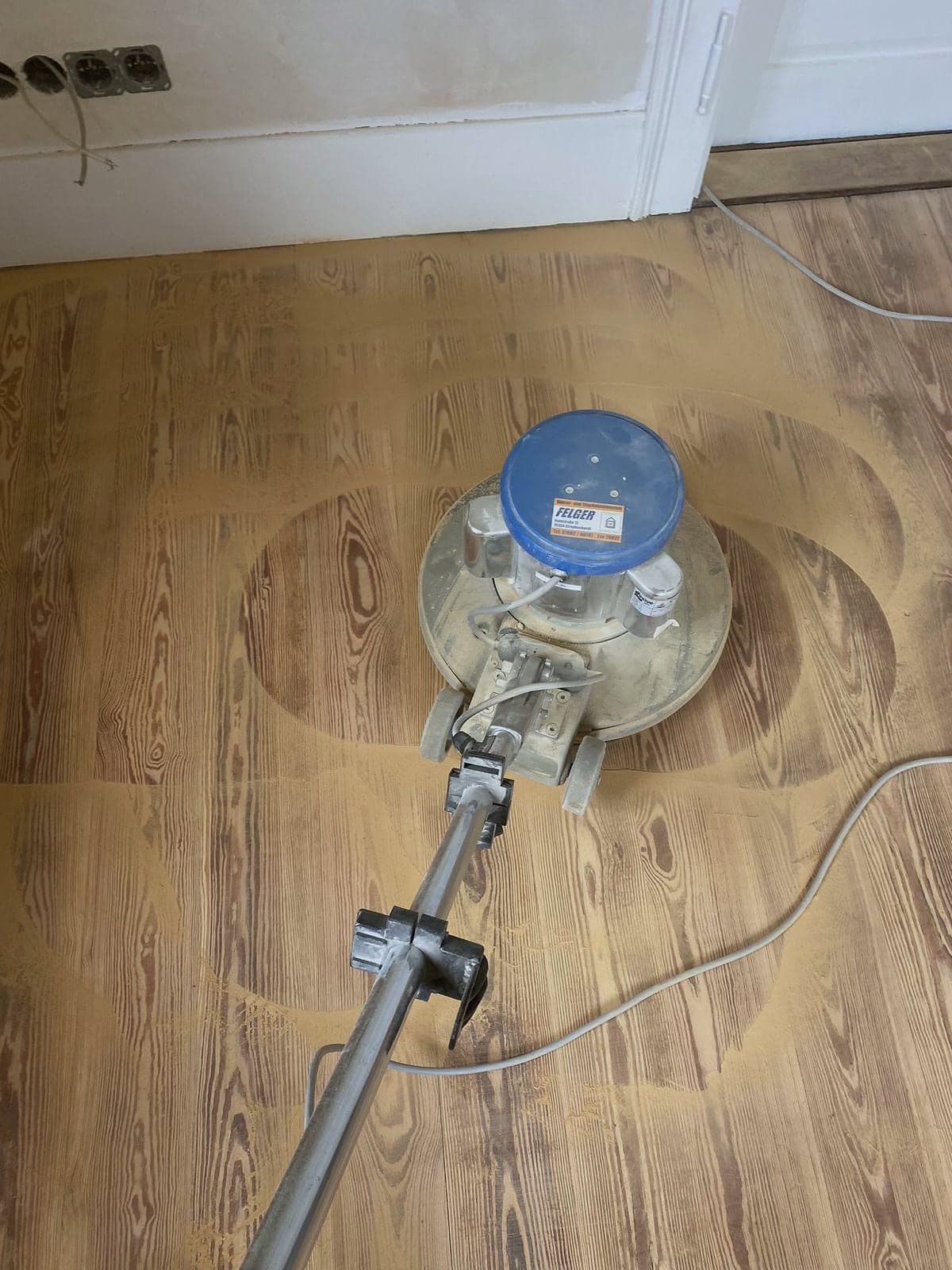 Tellerschleifer von oben auf einem Altbau-Dielenboden, die Schleifbahnen zeichnen sich als helle Bögen im Holz ab